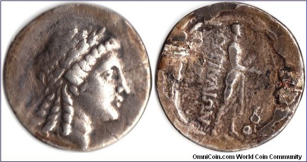 silver tetradrachm from the Aeolian city state of Myrina. Appollo laureate obverse. Statue of Apollo Gryneus standing with lustral branch and patera, omphalos and amphora at his feet. This example has been a jewelery piece and the reverse has significant wear. Still very collectable.