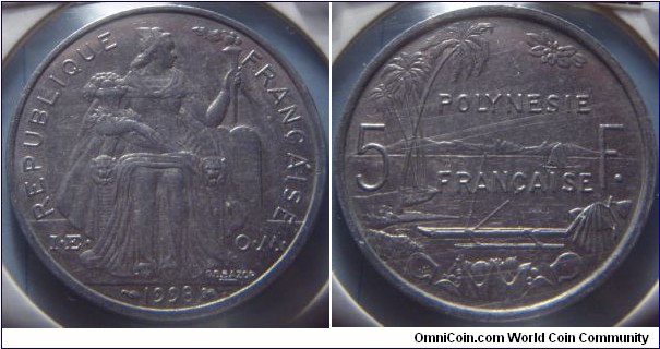 French Polynesia | 
5 Francs, 1998| 
31 mm, 3.8 gr. | 
Aluminium | 

Obverse: Seated Liberty on throne holding lit torch and assorted fruit facing right, date below | 
Lettering: REPUBLIQUE FRANÇAISE I•E • O•M• 1998 | 

Reverse: Palm trees on left, sailboat at sea min centre, mountains in distance. Boat with outrigger in foreground with assorted fruit in container, divide denomination| 
Lettering: POLYNESIE FRANÇAISE 5 F. |