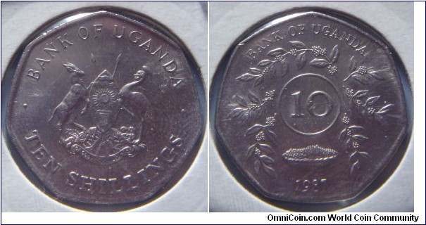 Uganda | 
10 Shillings, 1987 | 
26 mm, 5.7 gr. | 
Stainless Steel |  

Obverse: National Coat of Arms, denomination below | 
Lettering: • BANK OF UGANDA • TEN SHILLINGS | 

Reverse: Circle of sprigs, denomination middle, date below | 
Lettering: BANK OF UGANDA 10 1987 |