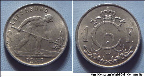 Luxembourg | 
1 Franc, 1947 | 
23 mm, 5 gr. | 
Copper-nickel | 

Obverse: Man shoveling coal, date belown | 
Lettering: LETZEBURG 1947 |

Reverse: Crowned Charlotte Monogram divides denomination | 
Lettering: Ch 1F. |