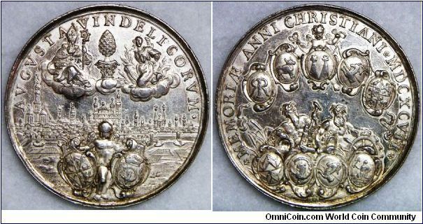 German States - Augsburg, Reichsstadt Silbermedaille (Silver medal), 1697. City view of East, about that St. Ulrich and St. Afra, between them Stadtpyr, below genius with the crests of the city caretaker white and Imhof / angel the crests of the five secret long coat, Rehm, Rehlinger, Stetten and Aman holds at a volume, under that the river Gods Lech and Wertach with the crests of the master builder Ilsung, Imhof, Stetten and Voith of the mountain. 44 mm, 29.29 g. Very rare.